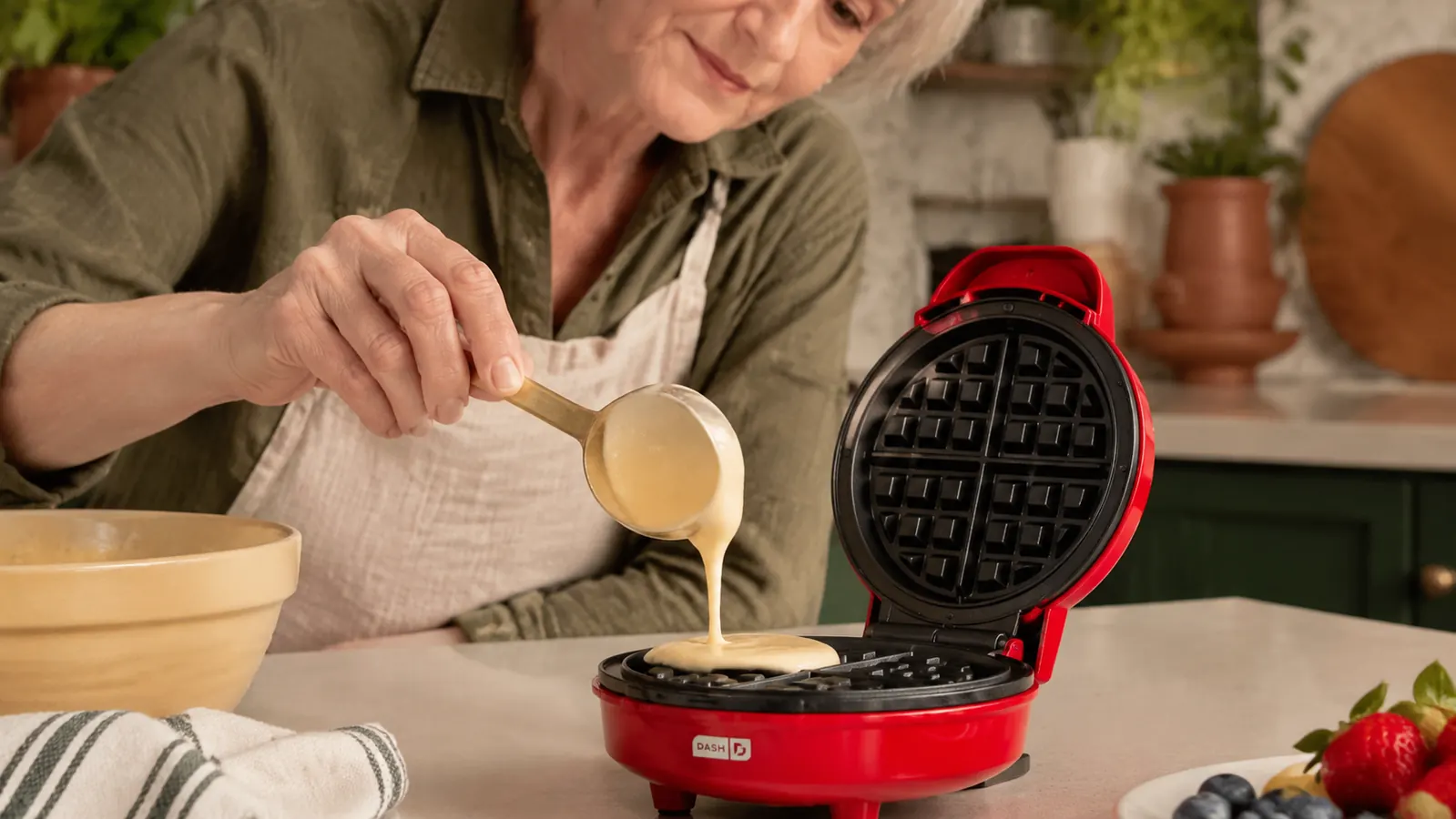 Hand pouring waffle batter into the open Dash mini waffle maker