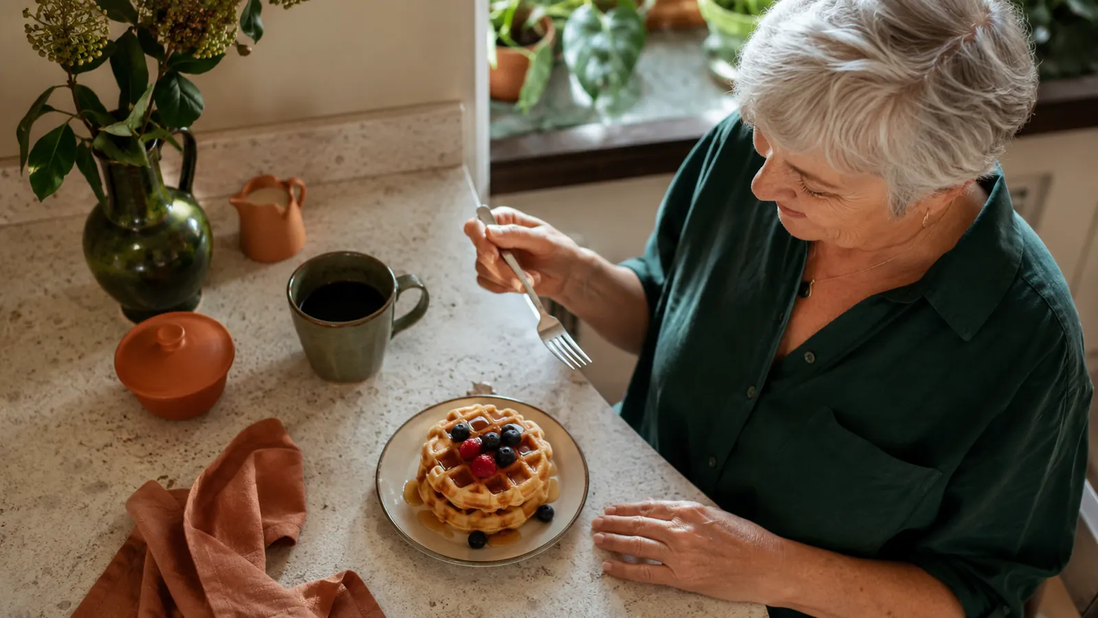 A single stacked mini waffle topped with berries and syrup on a small plate next to a coffee cup