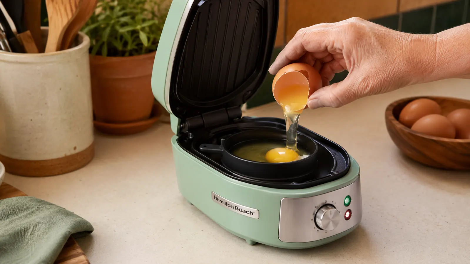 Hamilton Beach breakfast sandwich maker open on a counter with an egg cooking inside the ring