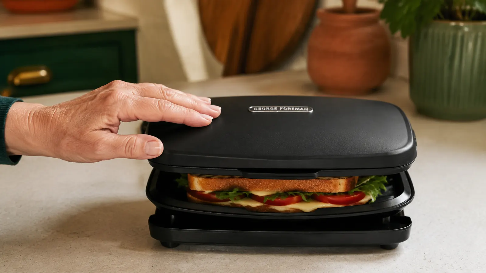 Hand closing the lid of a compact George Foreman mini grill over a buttered sandwich